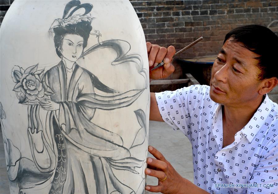 Imagen del 28 de junio de 2016 del artista folclórico Yang Minsheng pintando sobre una obra de porcelana azul y blanca, en la zona turística de Yaotou Kiln en el municipio de Yaotou del condado de Chengcheng, provincia de Shaanxi, en el noroeste de China.El sitio de antiguos hornos populares, cubriendo un área de cuatro kilómetros cuadrados, tiene una historia de elaboración de productos de cerámica de más de mil a?os. La técnica de elaboración de cerámica en Yaotou Kiln fue incluida en el Patrimonio Nacional Cultural Intangible en el 2006. (Xinhua/Tao Ming)