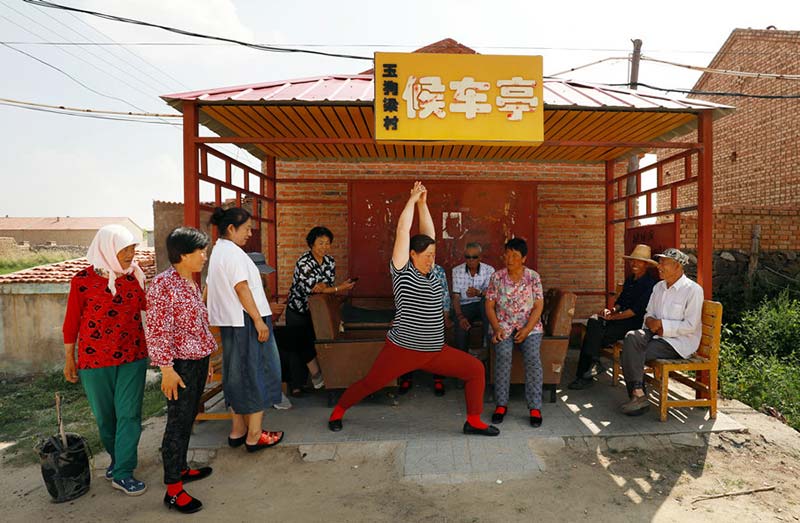 Residentes ense?an habilidades del "Yoga de Yugouliang" mientras esperan el autobús. [Foto: Zhu Xingxin/China Daily]