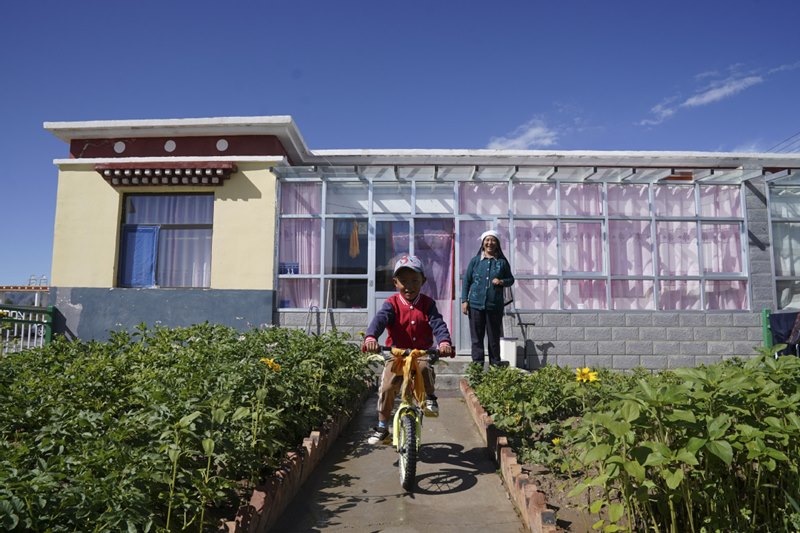 Dorje Changje, de seis a?os, monta en bicicleta frente a su nueva casa en una aldea de reasentamiento en Qabqa, condado Gonghe, el 17 de agosto de 2020. [Foto de Feng Yongbin / China Daily]