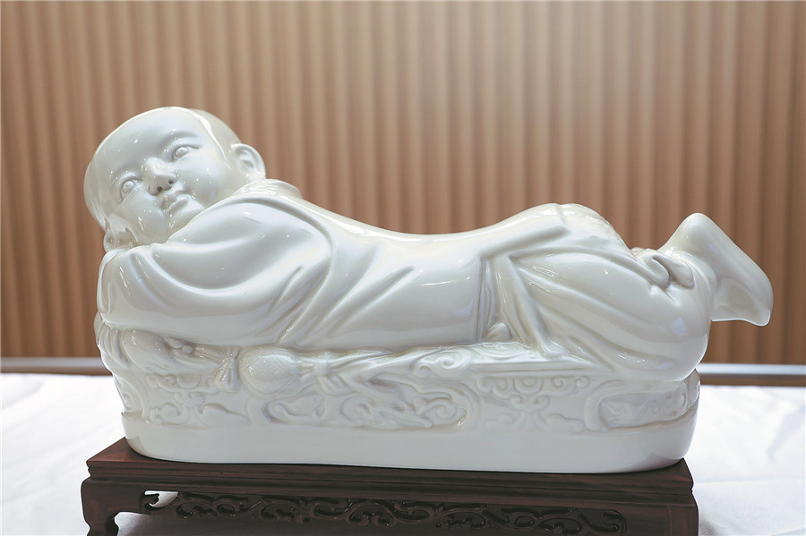 Almohada antigua de vidrio blanco con forma de bebé acostado en una cama alargada. Esta almohada de porcelana es de la dinastía Song del Norte y se encuentra en el Museo del Palacio Imperial de Beijing. [Foto: proporcionada a China Daily]