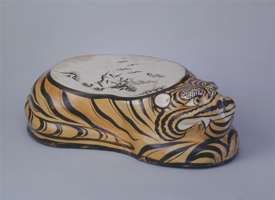 Una almohada pintada en forma de tigre con esmalta marrón. La espalda del tigre sirve como superficie de almohada, con un fondo blanco y una pintura que representa aves de oto?o en un pantano de juncos. [Foto: Sitio web oficial del Museo del Palacio Imperial de Beijing]