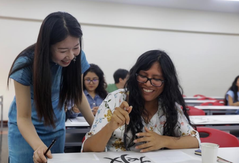 Imagen del 22 de abril de 2025 de la profesora, Liang Qing (i), del Instituto Confucio de la Pontificia Universidad Católica del Perú (PUCP), instruyendo a una alumna durante un taller de caligrafía china en el marco de la celebración del Día Internacional de la Lengua China, en la Pontificia Universidad Católica, en Lima, Perú. (Xinhua/Mariana Bazo)