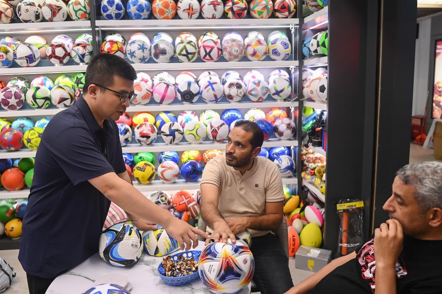 Un empresario presenta productos relacionados con el fútbol a dos clientes extranjeros en Yiwu, en la provincia oriental china de Zhejiang, el 30 de mayo de 2024. (Xinhua/Huang Zongzhi)